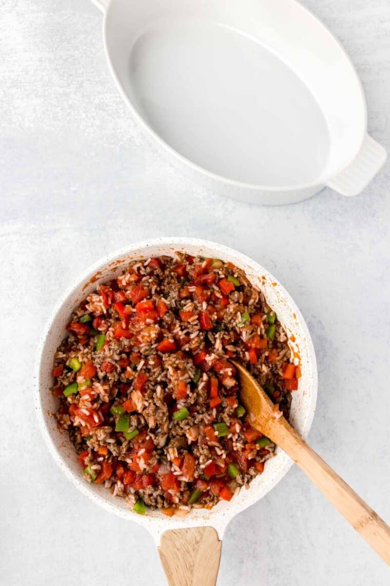 A bowl of filling for unstuffed pepper casserole is stirred with a wooden spoon.