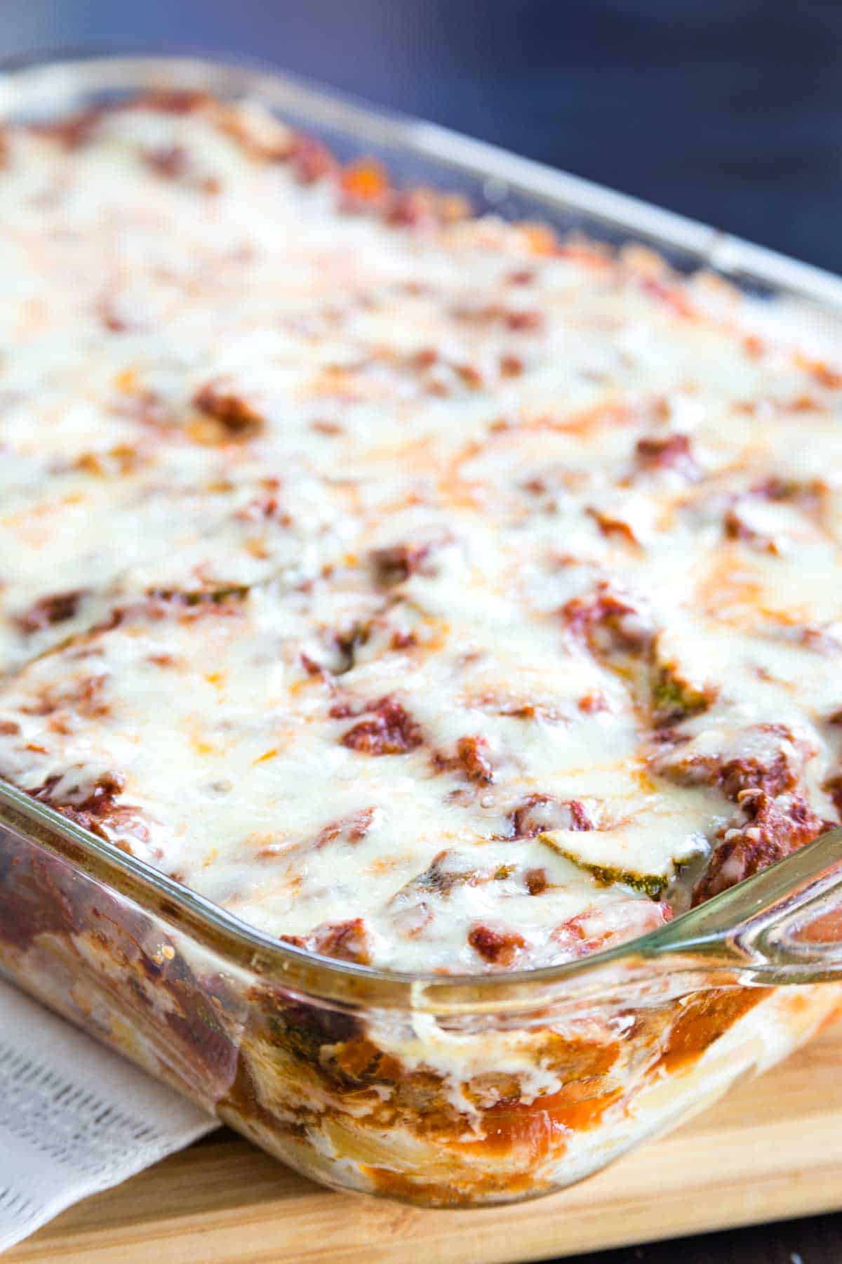 A glass baking pan of cheese-topped Italian noodle casserole.