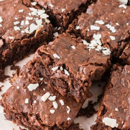 Cut protein brownies are shown on a piece of parchment paper and topped with coconut.
