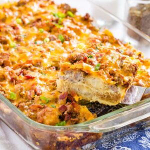A slice of tater tot breakfast casserole being lifted out of a glass baking dish with a spatula.