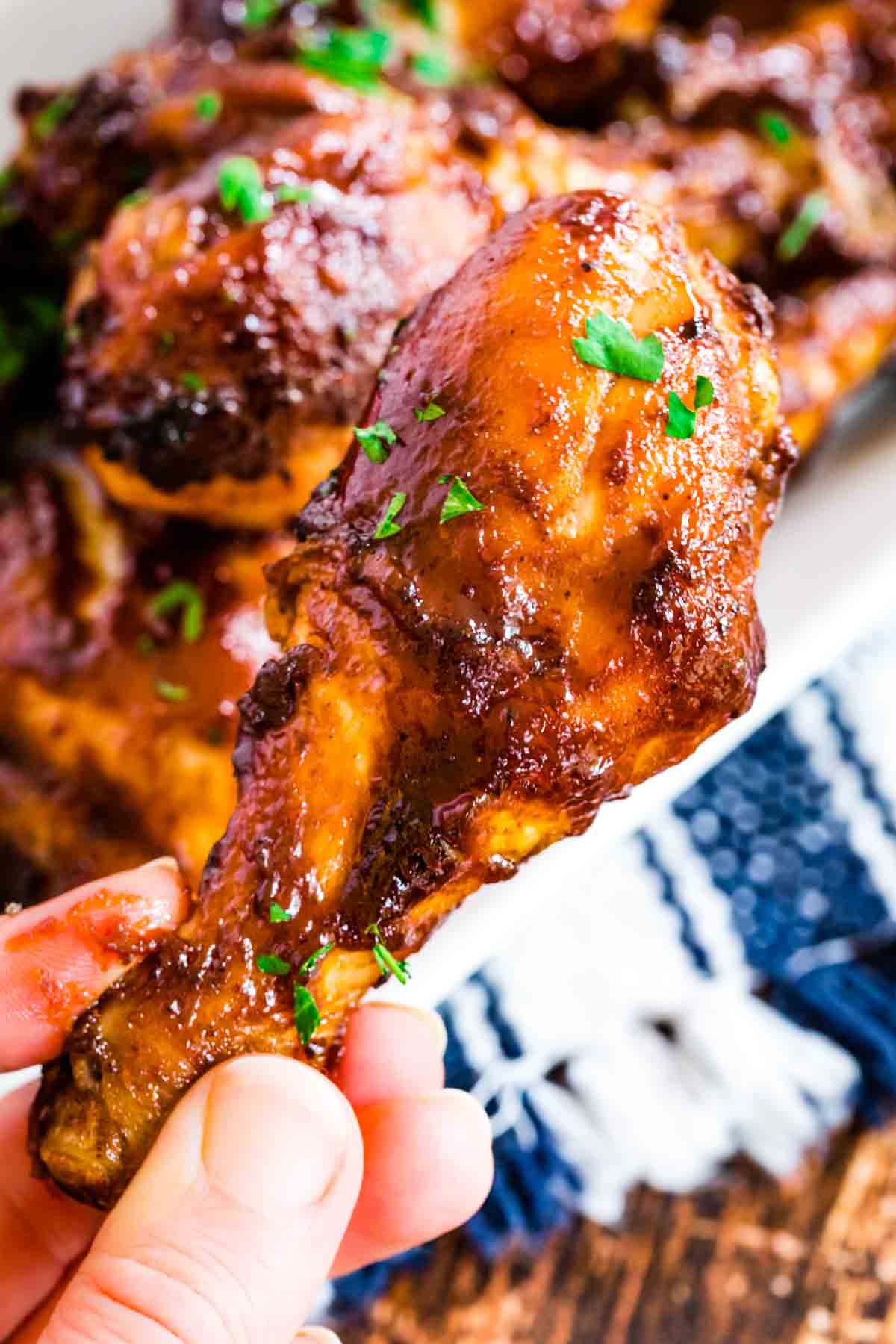 A hand holds an air fryer bbq chicken leg garnished with parsley leaves.