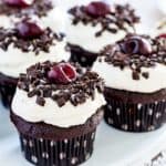 A platter of chocolate cupcakes in polka dot wrappers topped with whipped cream, chocolate shavings, and a cherry with text overlay that says "Gluten Free Black Forest Cupcakes".