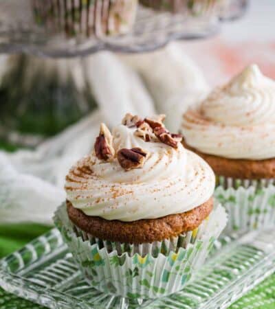 Carrot cake cupcakes frosted with cream cheese frosting are garnished with pecans.