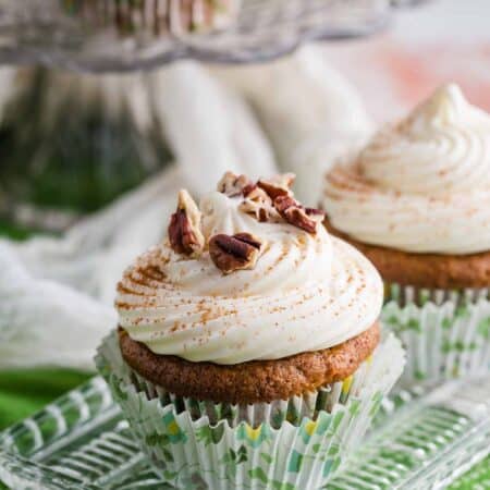 Carrot cake cupcakes frosted with cream cheese frosting are garnished with pecans.