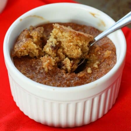 A spoon digs into a ramekin of chocolate chip cookie in a mug on a red background.