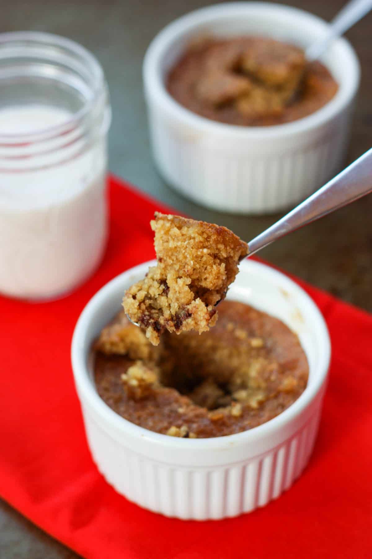 A spoon lifts out a bit of chocolate chip cookie in a mug from a white ramekin.