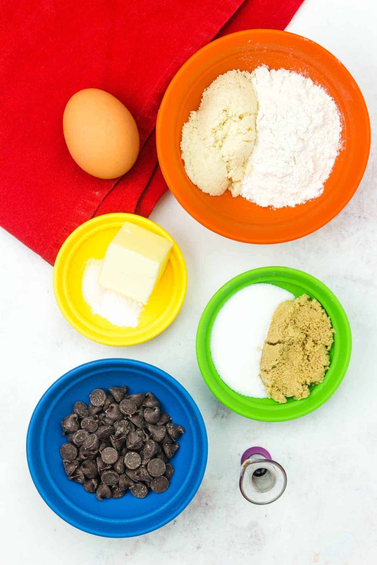 The ingredients for chocolate chip cookie in a mug are shown portioned out: melted butter, sugar, brown sugar, vanilla, egg, oat flour, almond meal, salt, baking powder, chocolate chips.