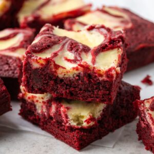 Two stacked red velvet brownies with more scattered around them.