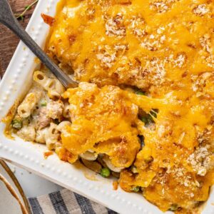 A serving spoon in a baking dish of cheese-topped tuna noodle casserole.