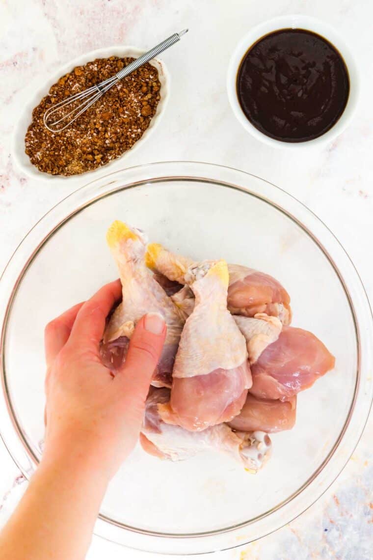 A hand helps to coat the chicken with oil.
