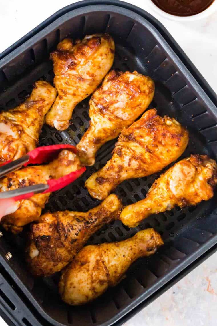 Tongs turn over chicken legs in an air fryer.