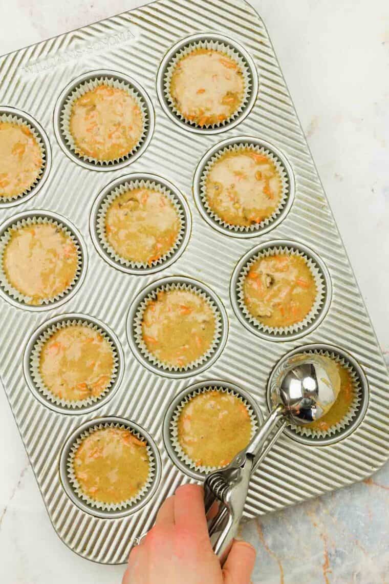 A muffin scoop portions out batter into a cupcake tin.