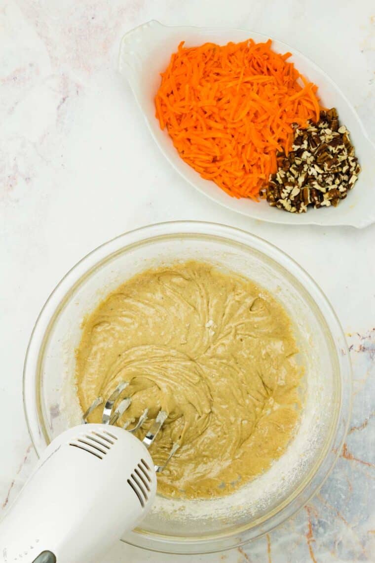 A hand mixer blends the batter for carrot cake cupcakes.