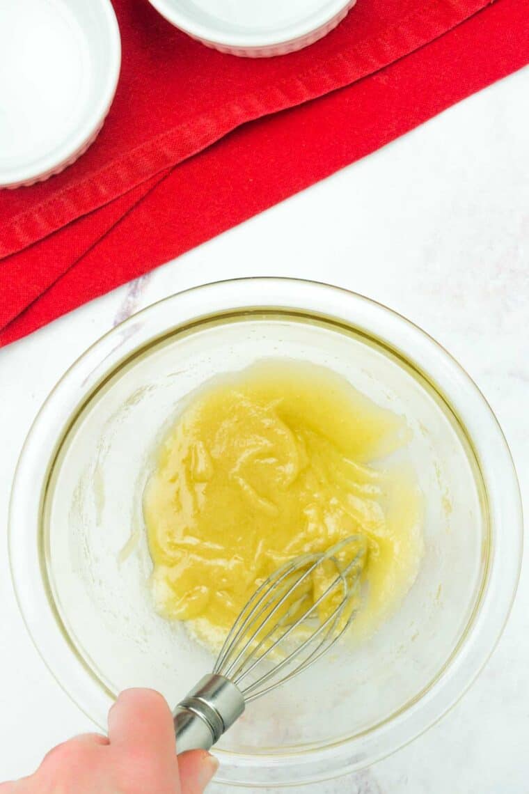 Melted butter and sugar is whisked in a glass bowl.