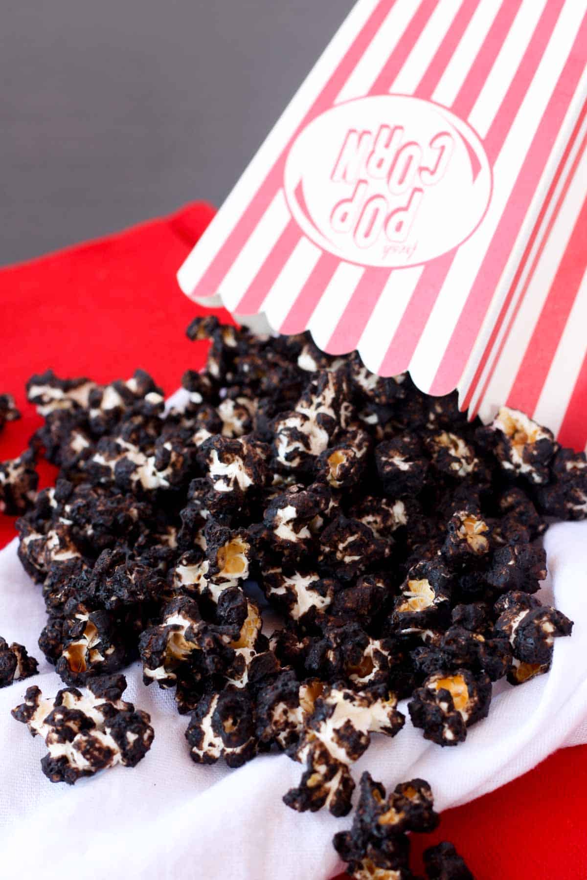 A striped popcorn box tipping upside down to spill out the Mexican hot chocolate popcorn inside.