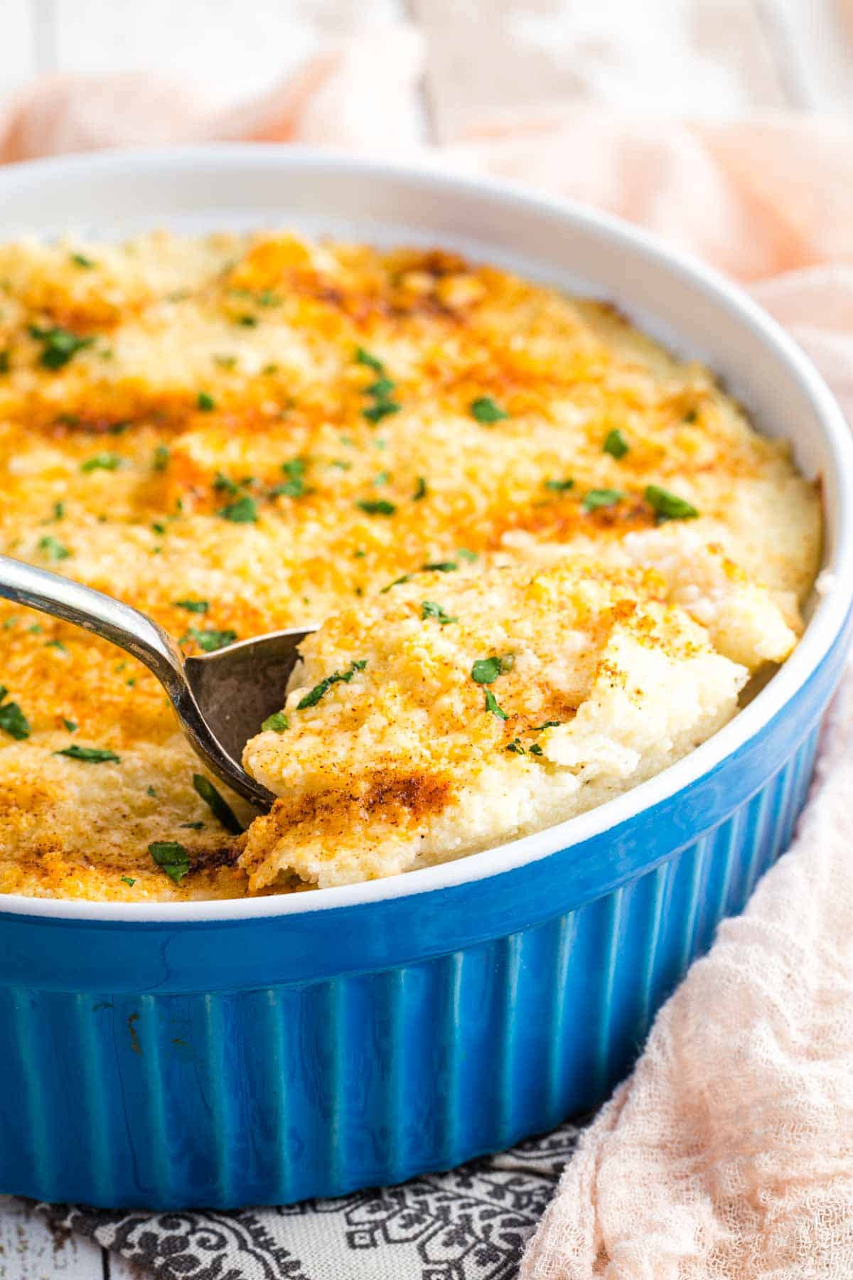 A spoon dips into a blue casserole dish filled with whipped cauliflower.