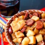A glass of red wine is shown behind a bowl of potatoes and chorizo for patatas riojana.