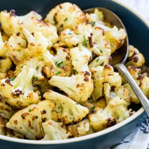 Roasted cauliflower in a blue dish with a serving spoon.