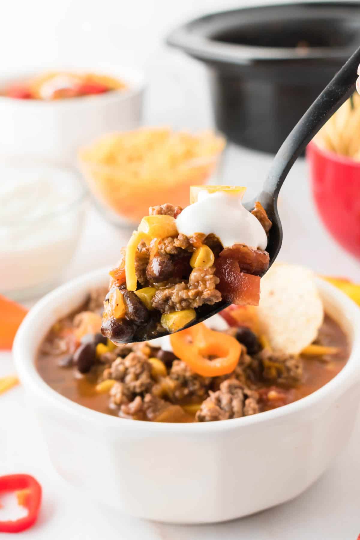 A spoon shows a portion of taco soup held above a white bowl of soup.