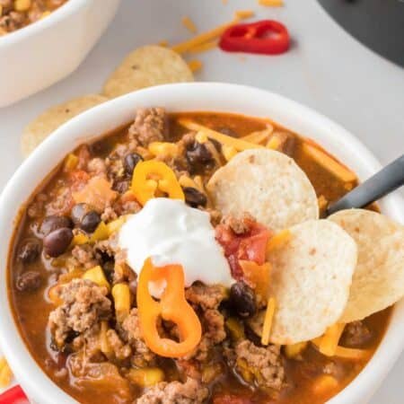 A white bowl brims with cheese and sour cream-topped taco soup that's garnished with corn chips.