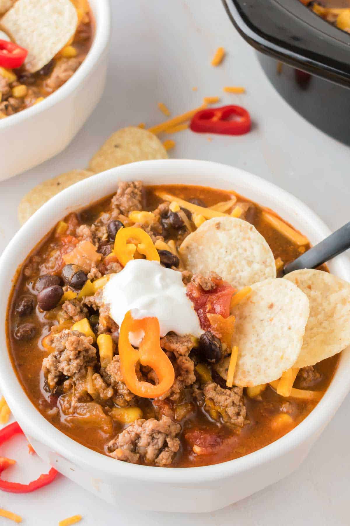 A white bowl brims with cheese and sour cream-topped taco soup that's garnished with corn chips.