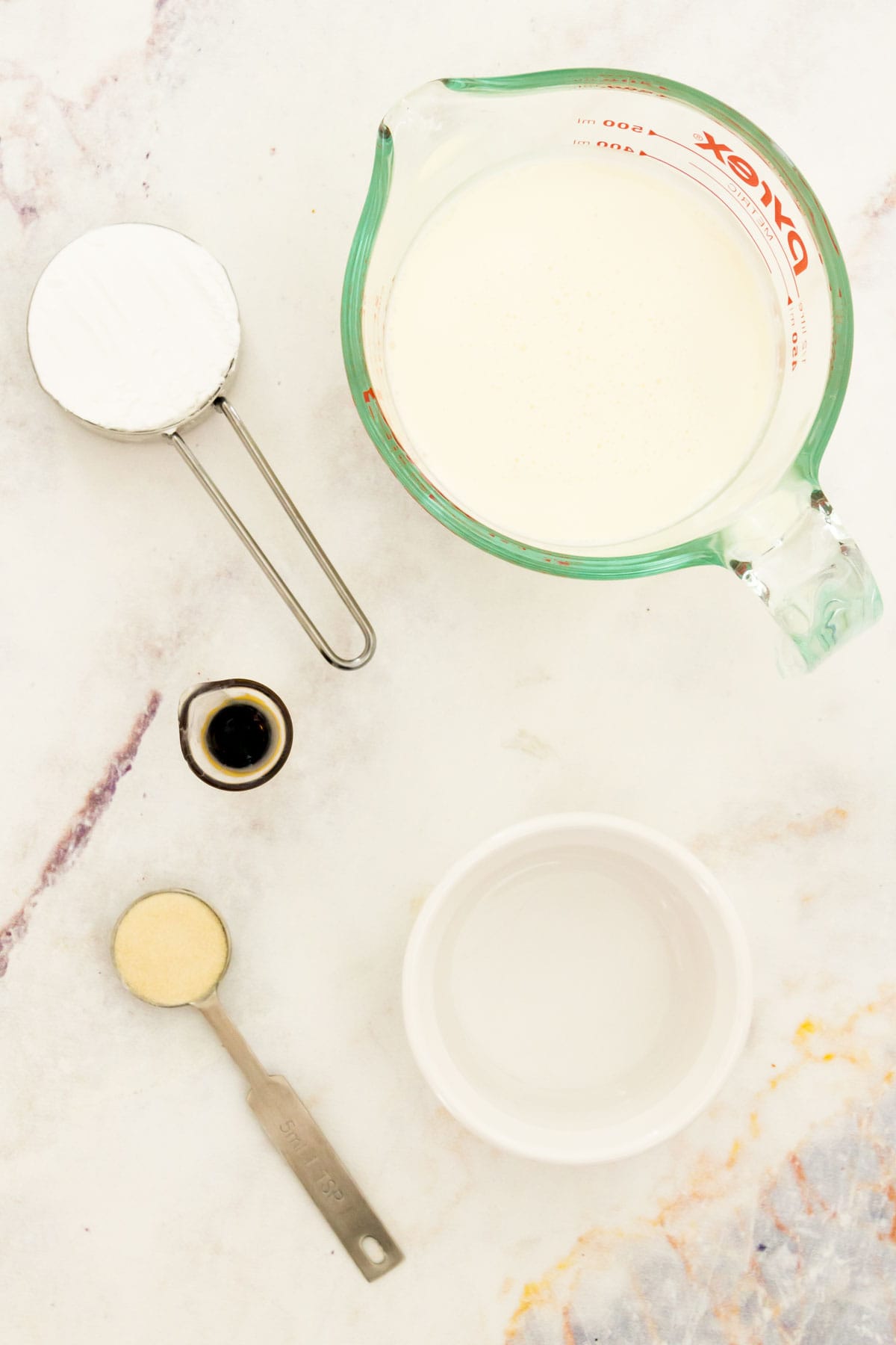 Bowls and measuring spoons of whipped cream frosting ingredients.