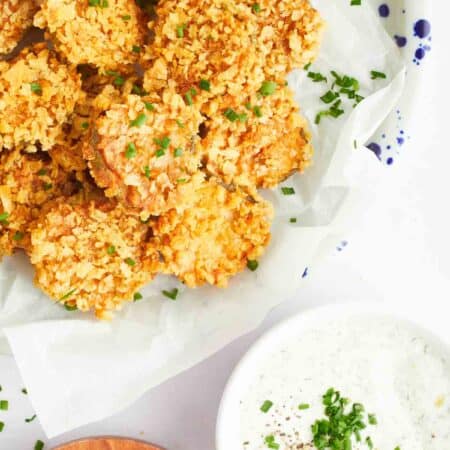 Potato chip-coated air fryer fried pickles on a serving platter next to a bowl of ranch.