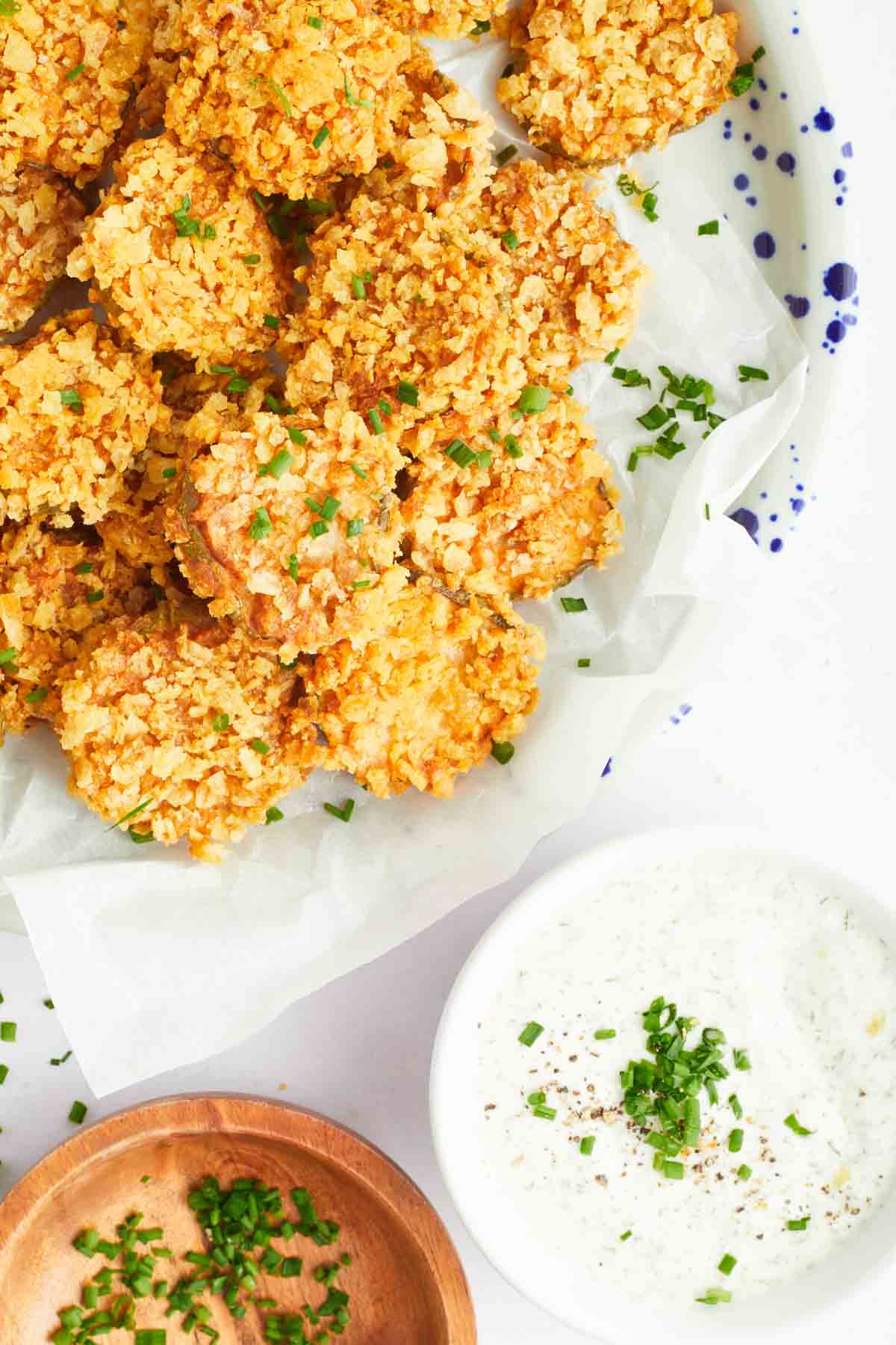 Potato chip-coated air fryer fried pickles on a serving platter next to a bowl of ranch.