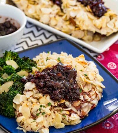 A plate of almond crusted chicken topped with cherry balsamic sauce with more chicken pieces seen in the background.