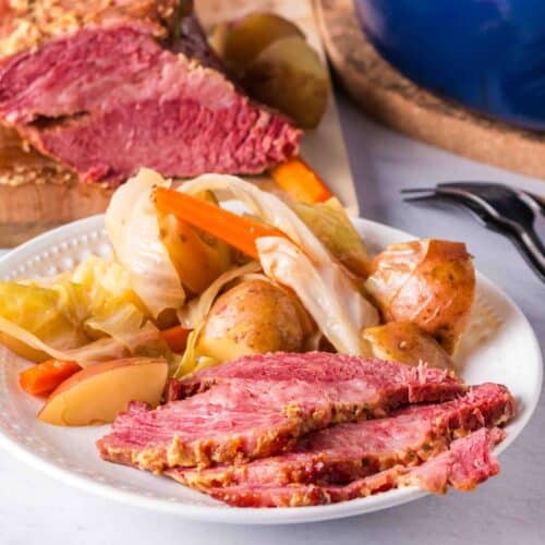 Slices of corned beef served on a plate with cabbage, potatoes, and carrots.