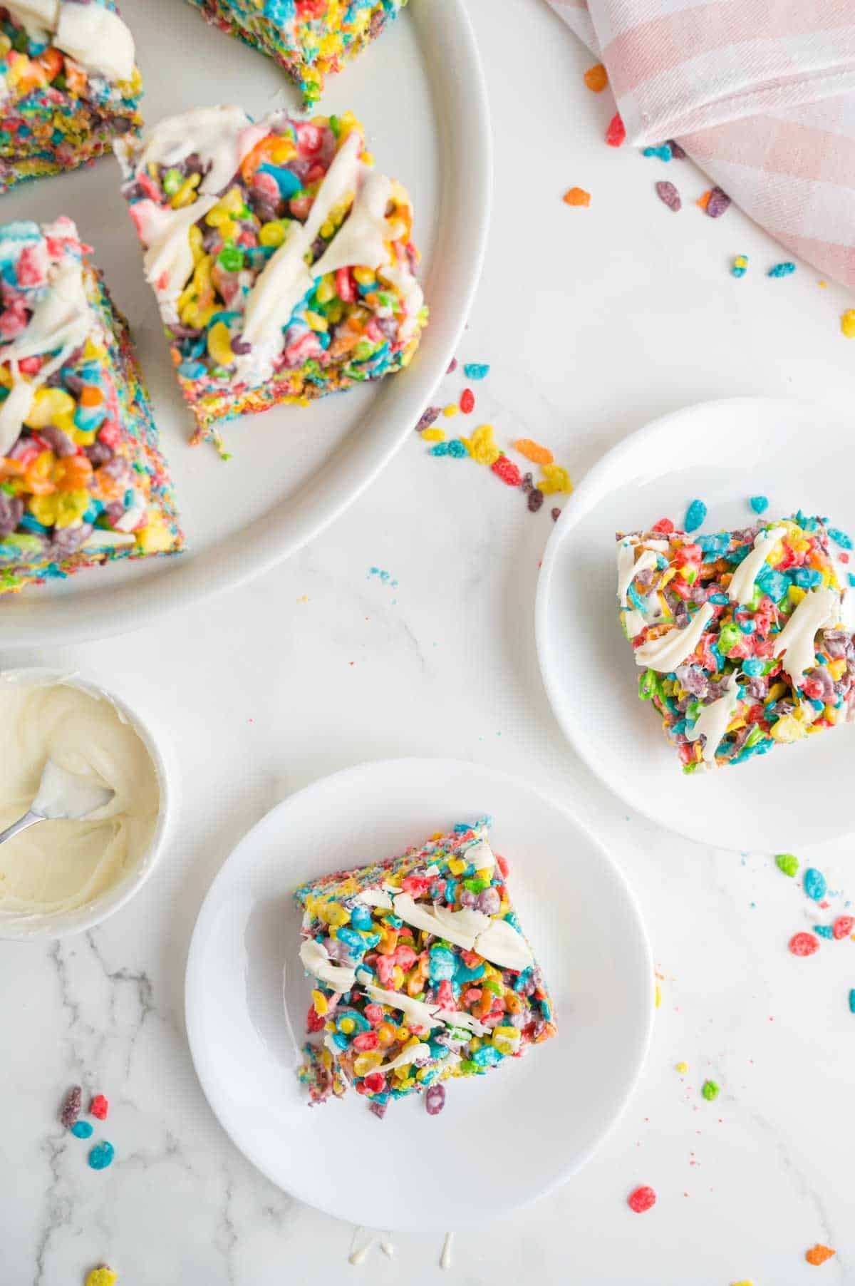 Two plates hold fruity pebbles treats with a plate of treats nearby.
