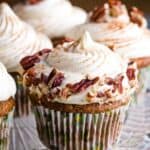 Carrot cupcakes with cream cheese frosting and chopped pecans on a glass platter with text overlay that says "Gluten Free Carrot Cake Cupcakes".