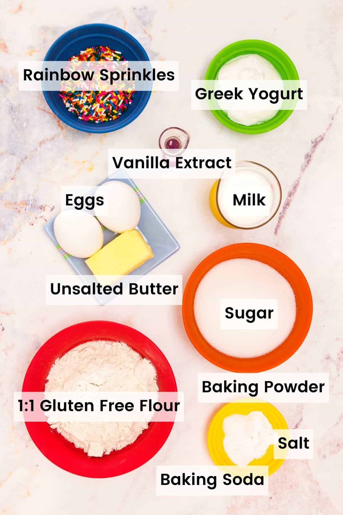 The ingredients for funfetti cupcakes are shown: gluten free flour, sugar, eggs, butter, baking powder and baking soda, salt, vanilla, buttermilk, rainbow sprinkles.
