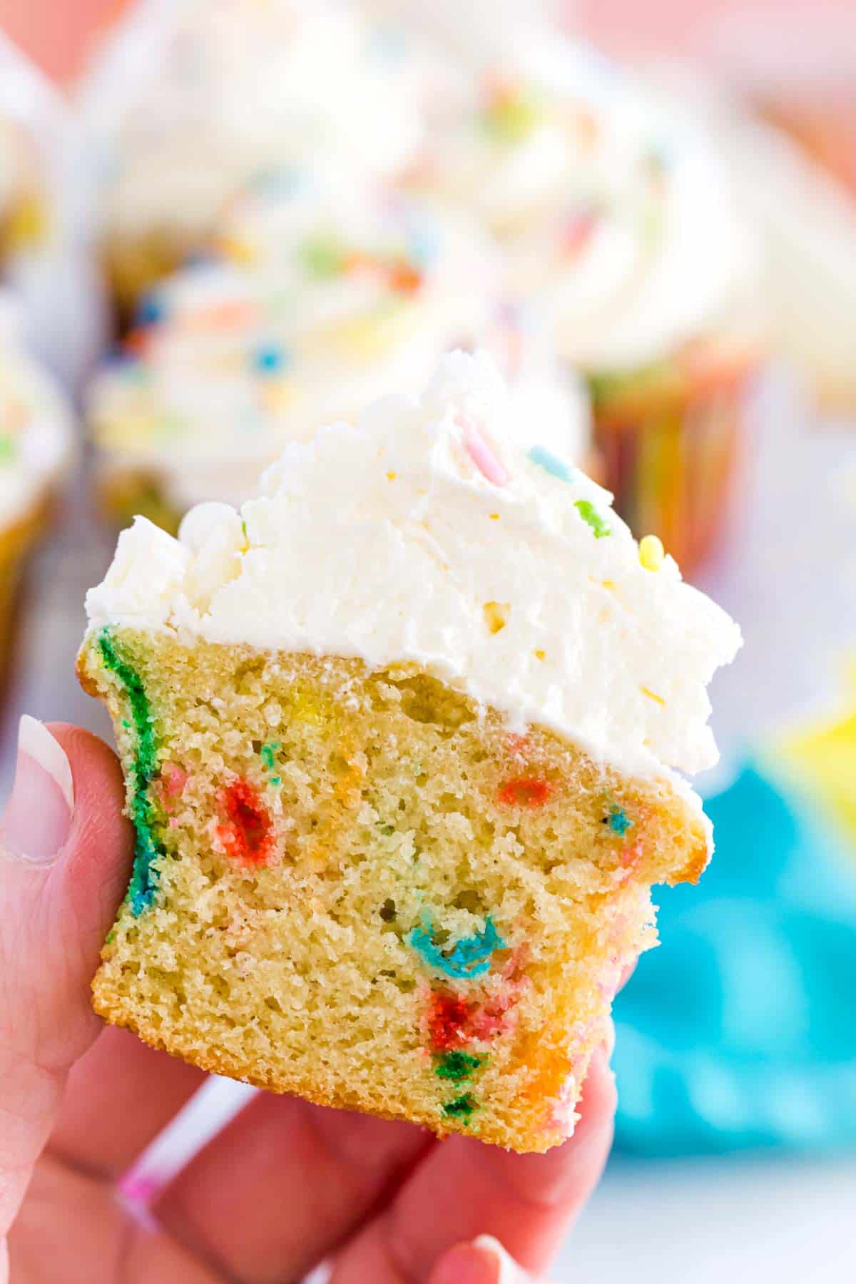 A hand holds a funfetti cupcake that's been cut in half to show the interior sprinkles.