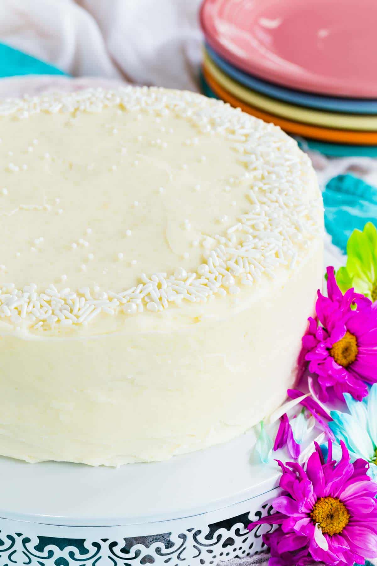 A gluten free white cake surrounded by bright flowers.