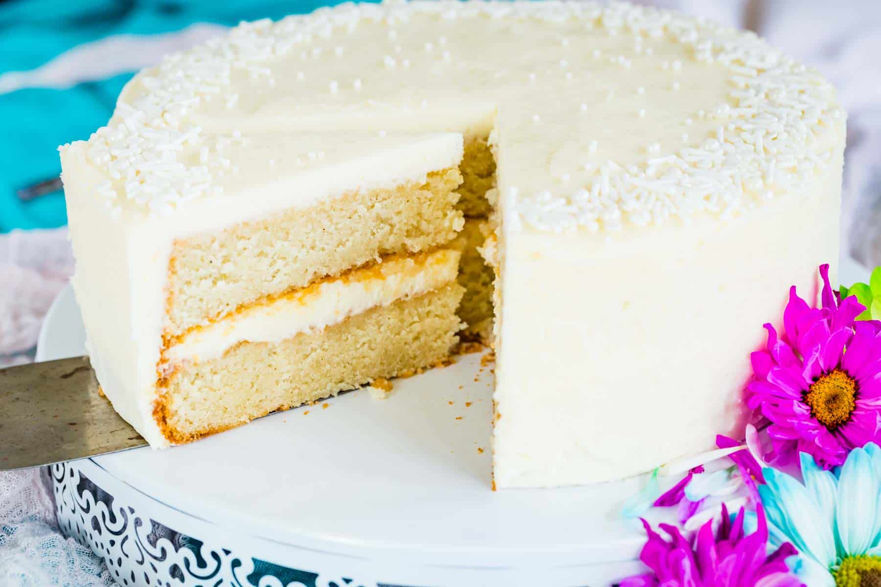 A piece of gluten free white cake is cut from the whole cake.