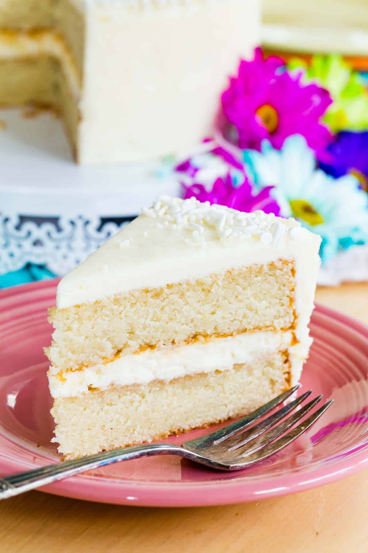 A fork rests on a pink plate next to a piece of gluten free white cake.