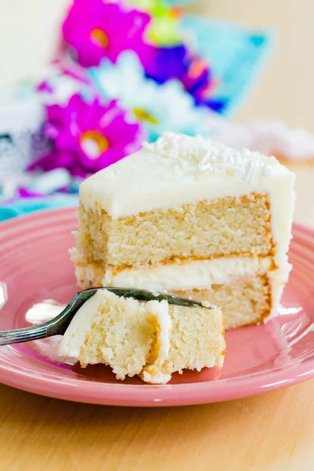 A fork cuts a bite of gluten free white cake from a slice of cake.