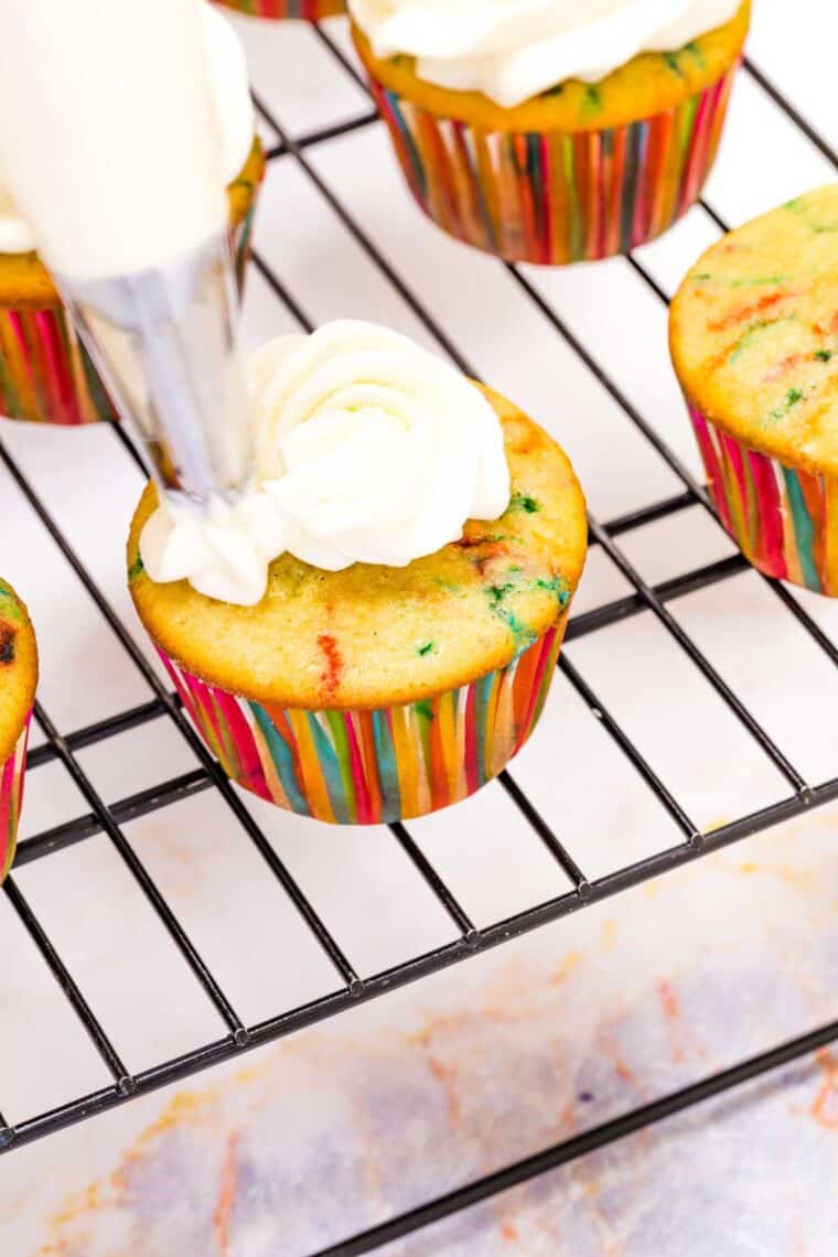 Frosting is added to funfetti cupcakes.