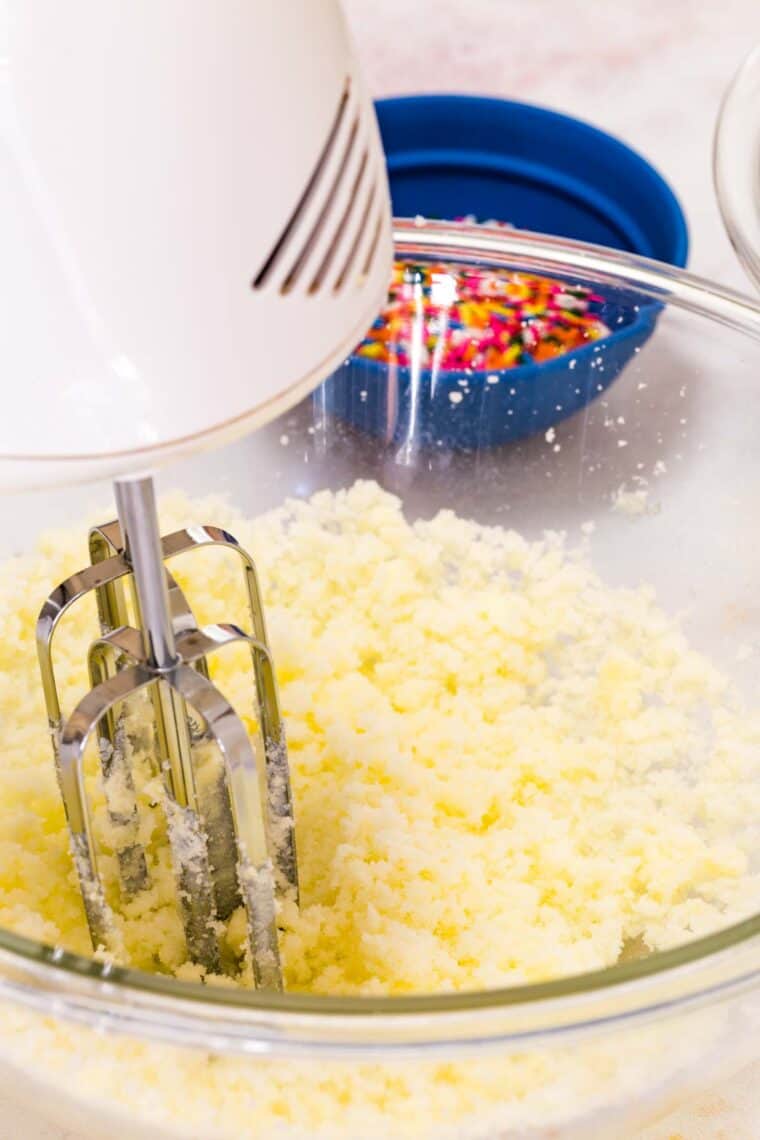 A hand mixer creams butter and sugar in a bowl.