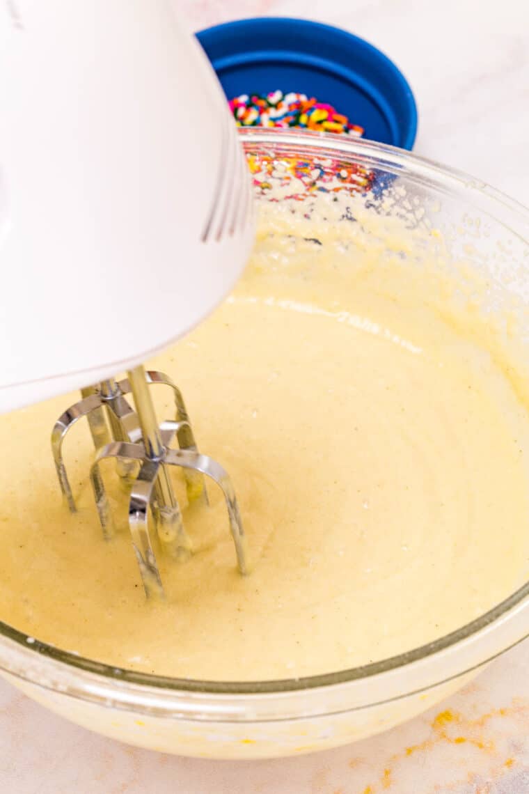 A hand mixer mixes a bowl of funfetti cupcakes batter.