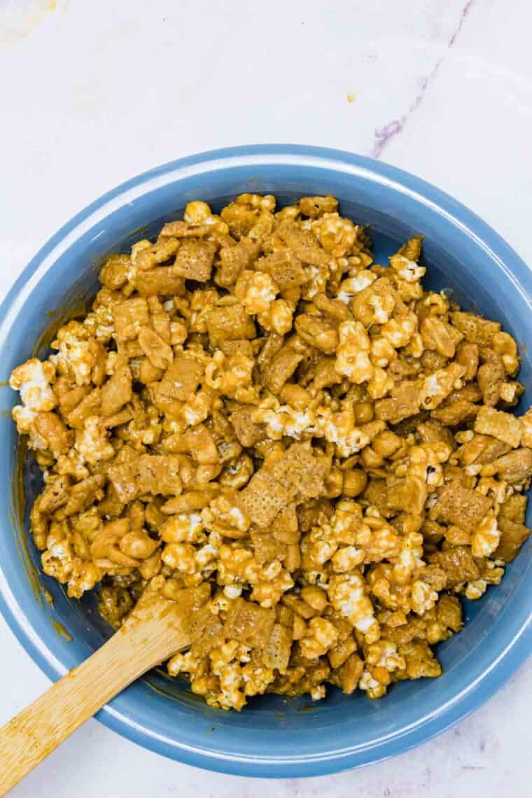 The popcorn mix is all combined in a bowl with wooden spoon.