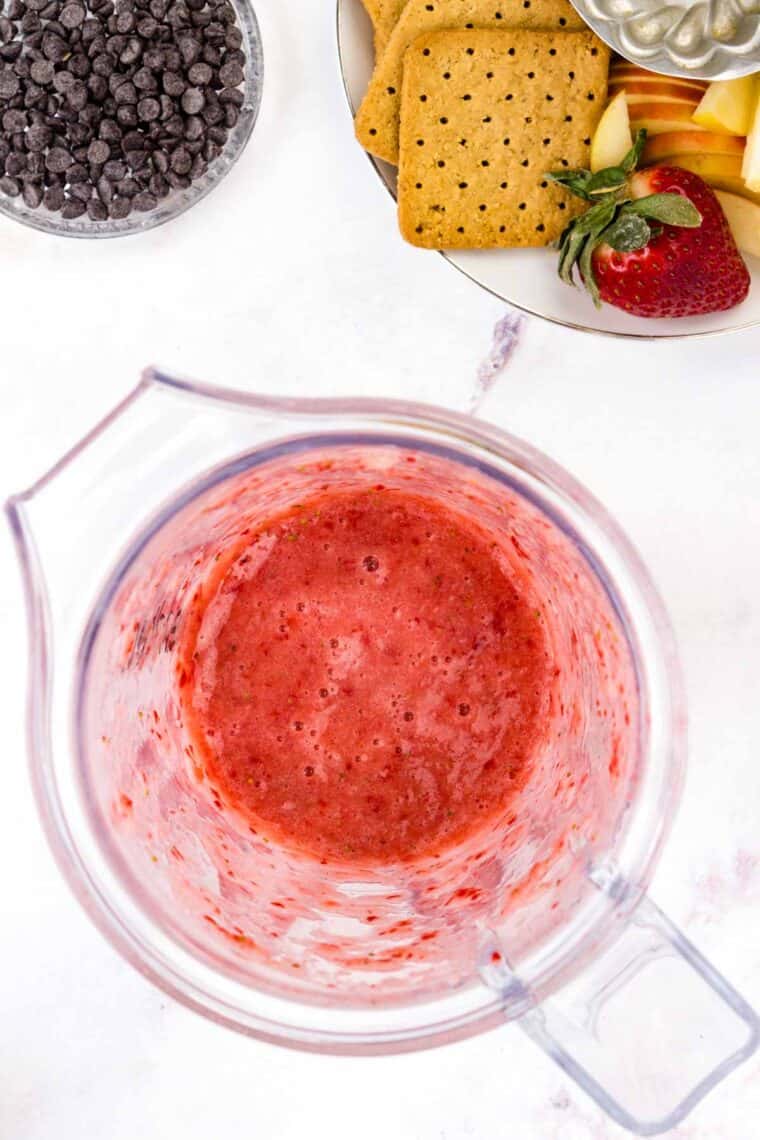 Bright pink strawberries are pureed in blender.