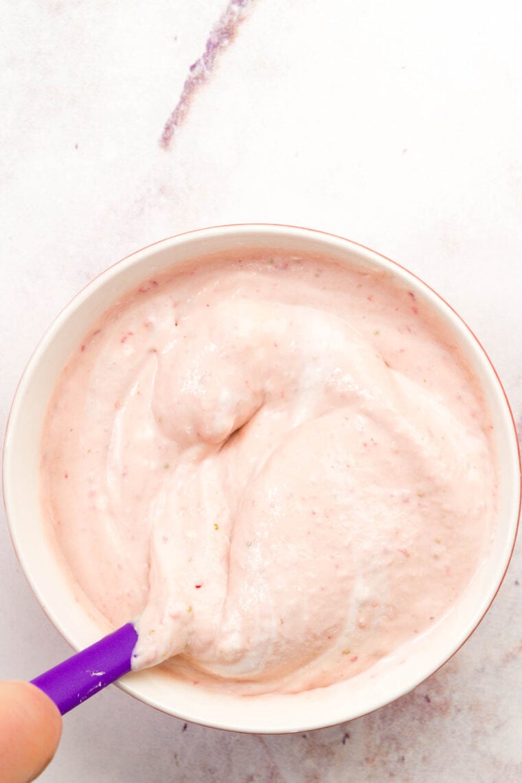 A spoon stirs a bowl of strawberry fruit dip together.