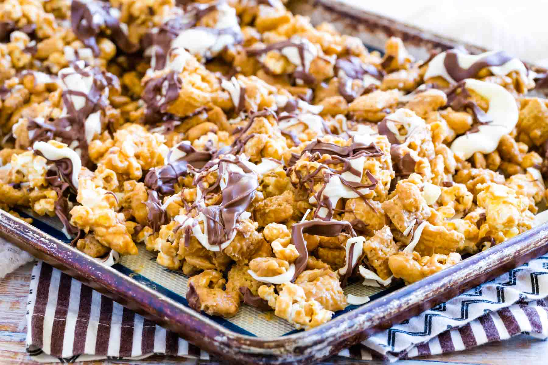 Melted chocolate tops a baking sheet filled with white chocolate popcorn.