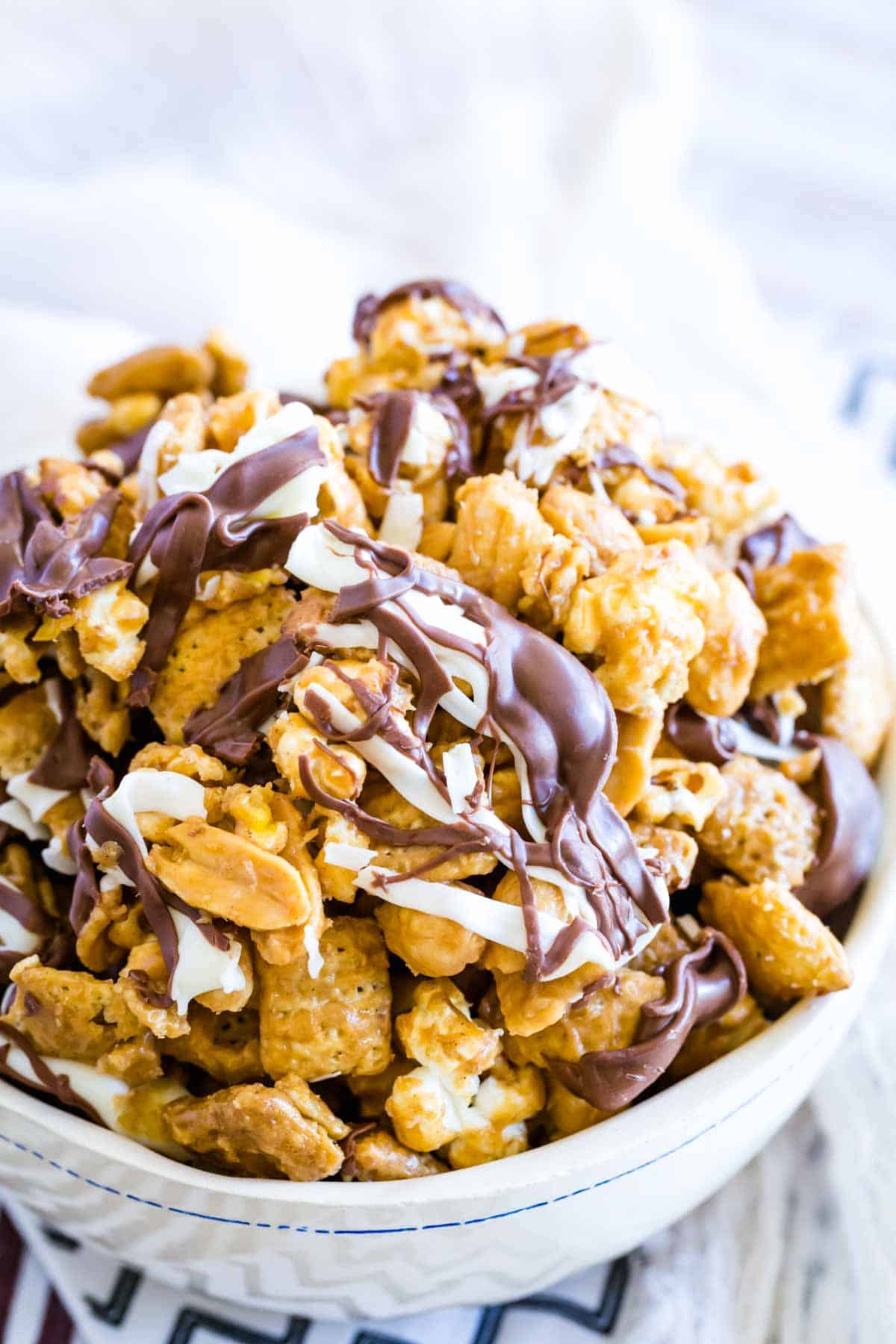 A white bowl holds chocolate-drizzled white chocolate popcorn.