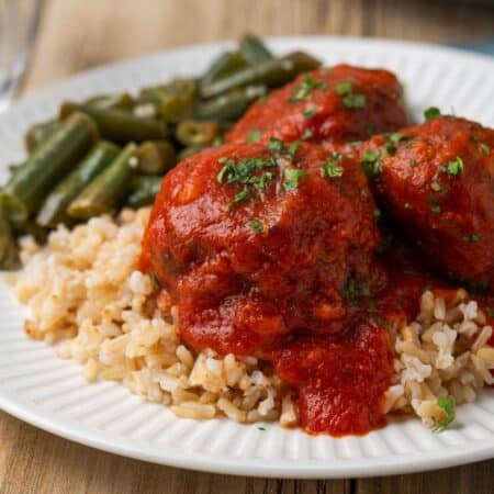 A plate of meatballs topped with sauce served over rice.