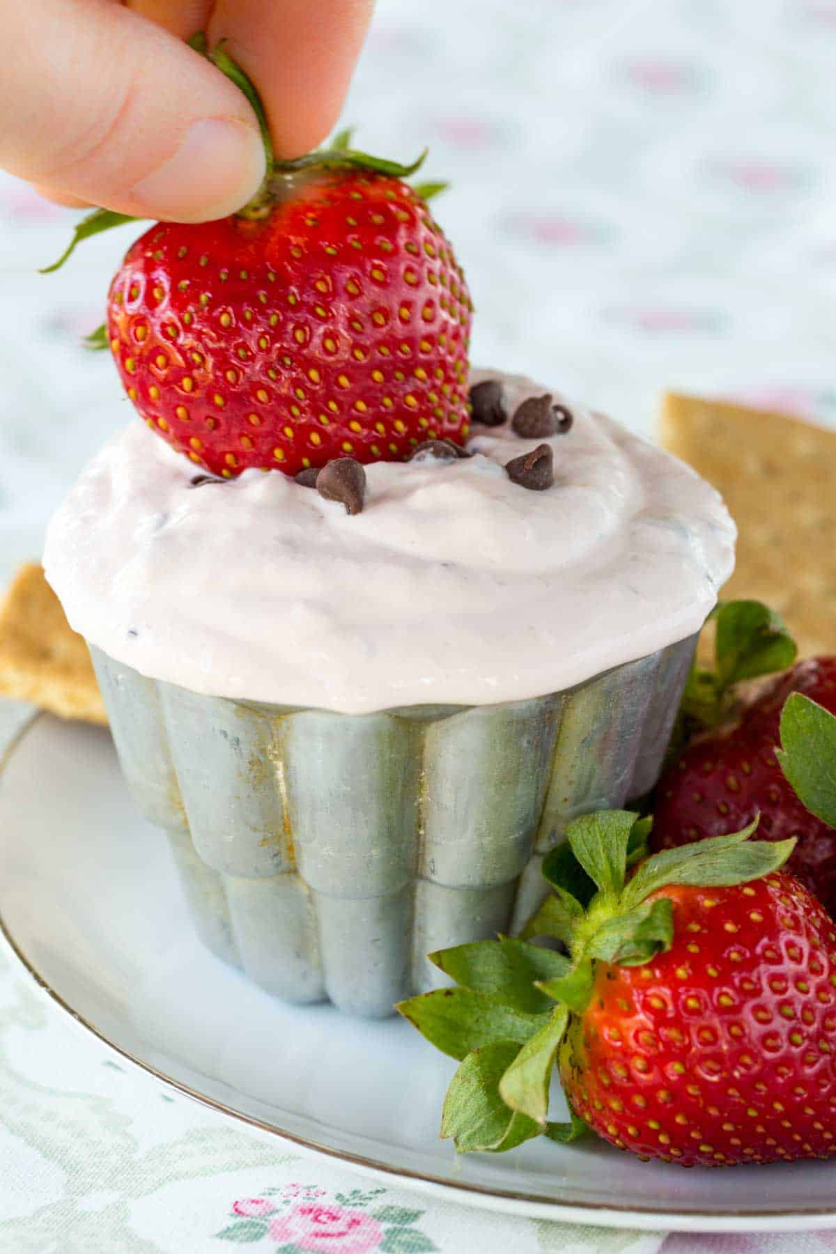 A hand dips a whole strawberry into strawberry fruit dip.