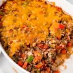 A cheese-topped ground beef and rice mixture in an oval baking dish with text overlay that says "Stuffed Pepper Casserole".