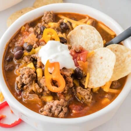 A bowl of taco soup topped with sour cream, cheese, pepper slices, and chips.